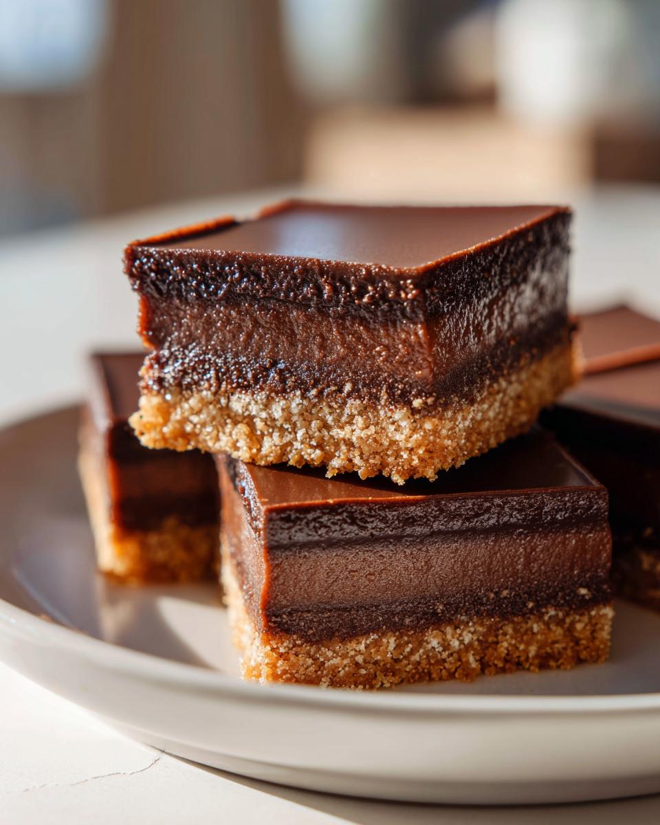 Close-up of rich chocolate dessert bars with a crumbly base stacked on a white plate.