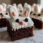 Square Easter bunny brownies topped with white frosting, marshmallow ears, and candy eyes and nose.