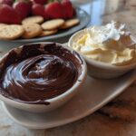Two bowls of easy dessert dips, one chocolate and one whipped cream, with crackers and strawberries in background.