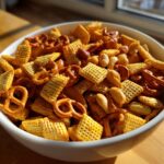White bowl filled with easy snack mix recipes including pretzels, nuts, and cereal pieces on wooden table