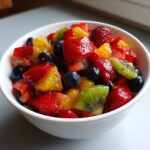 A white bowl filled with fresh fruit salad including strawberries, blueberries, kiwi, and orange pieces for fruit dessert recipes.