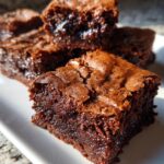 Close-up of rich, moist fudgy brownie recipes stacked on a white plate.