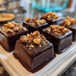 Close-up of homemade chocolate candy squares topped with chopped nuts on a white tray.