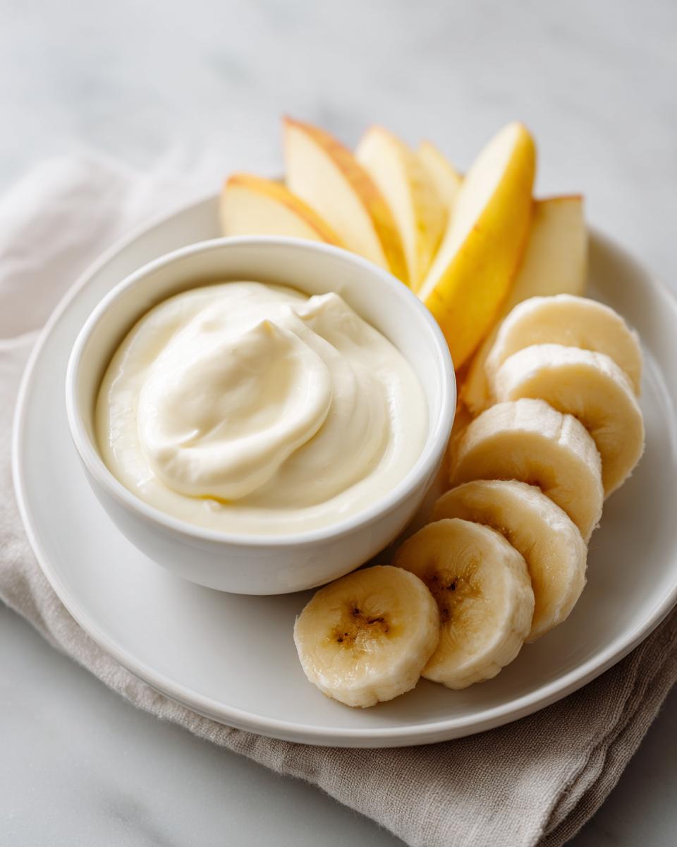 Plate with sliced bananas, apple wedges, and a bowl of creamy yogurt dip, a kid friendly snack recipes idea