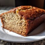 Close-up of a slice of moist banana bread on a white plate, perfect for beginner baking recipes.