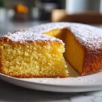 Slice of moist yellow cake dusted with powdered sugar on a white plate, showcasing easy cake recipes.