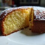 Close-up of a moist one bowl cake slice dusted with powdered sugar on a white plate.