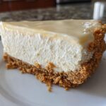 Close-up of a creamy slice of no bake cheesecake with graham cracker crust on a white plate.