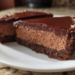 Close-up of a rich chocolate cheesecake slice with creamy filling and chocolate ganache topping.