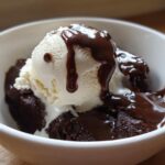Vanilla ice cream topped with simple chocolate sauce over a brownie in a white bowl.