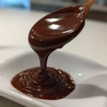 A spoon dripping smooth, glossy homemade ganache into a white dish