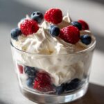 Glass cup filled with whipped cream topped with fresh raspberries and blueberries, a spring party dessert recipe