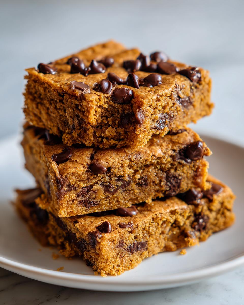 Three stacked chocolate chip cookie bars with melty chocolate chips on a white plate.